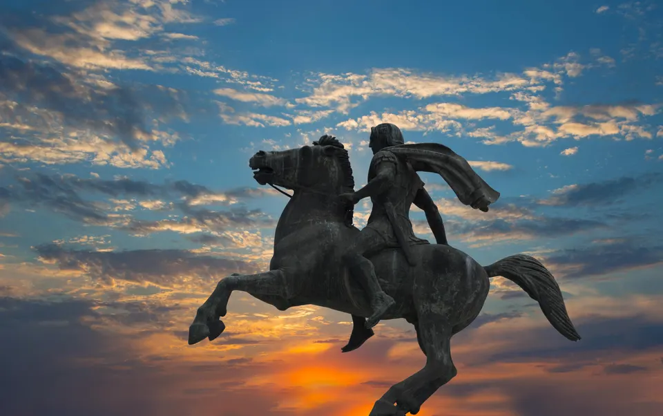 Bronze equestrian statue of a rider on a rearing horse silhouetted against a sunset sky.